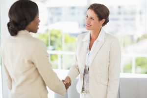 Two smiling businesswomen meeting and shaking hands in the office